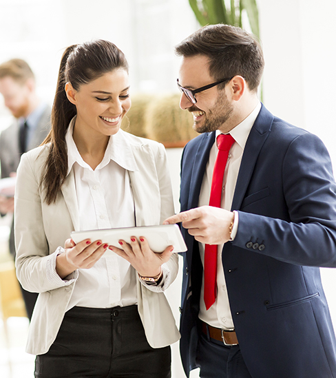 Young business couple working on tablet while other young business people talking in background